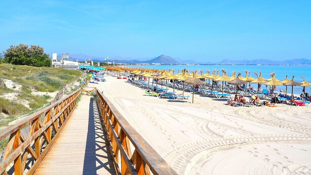 Una playa con un paseo marítimo de madera que lleva a sombrillas y sillas de playa.