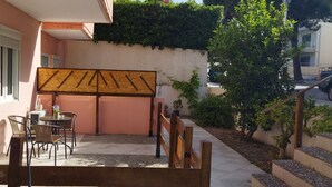 Ein Patio mit Tisch und Stühlen, eine hölzerne Bank und eine Mauer mit Kletterpflanzen.