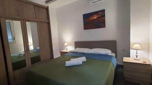 Ein ordentlich eingerichtetes Schlafzimmer mit Bett, Nachttischlampen, einem Nachttisch, einem Kleiderschrank und einem Bild an der Wand.