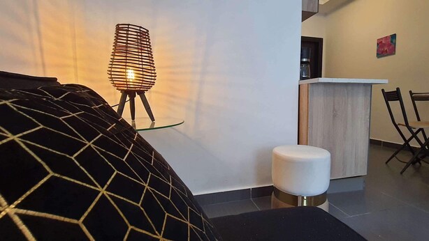 Ein modernes Wohnzimmer mit einem sofa in geometrischem Muster, einem kleinen runden Hocker, einem Couchtisch mit Glasplatte, einer ungewöhnlichen Drahtlampe, einer Holzkommode und einem Essbereich mit Tisch und Stühlen.