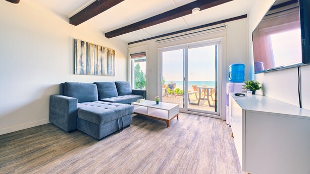A modern living room with a sectional sofa, a coffee table, and a sliding glass door leading to a balcony. - Suite 201: Beautiful 3-Bedroom Beachfront Townhouse (Wainfleet)