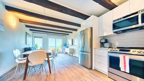 A modern kitchen with a built-in oven, microwave, and stainless steel refrigerator. There is a dining area with a table and chairs, and a large window providing a view of the outdoors. - Suite 201: Beautiful 3-Bedroom Beachfront Townhouse (Wainfleet)