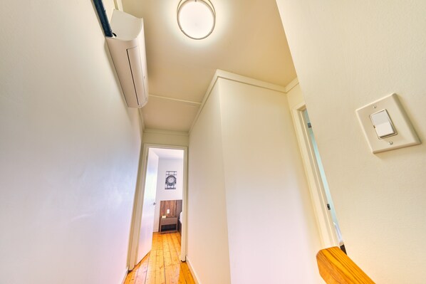 A narrow hallway with a wooden floor, white walls, and a ceiling light fixture.