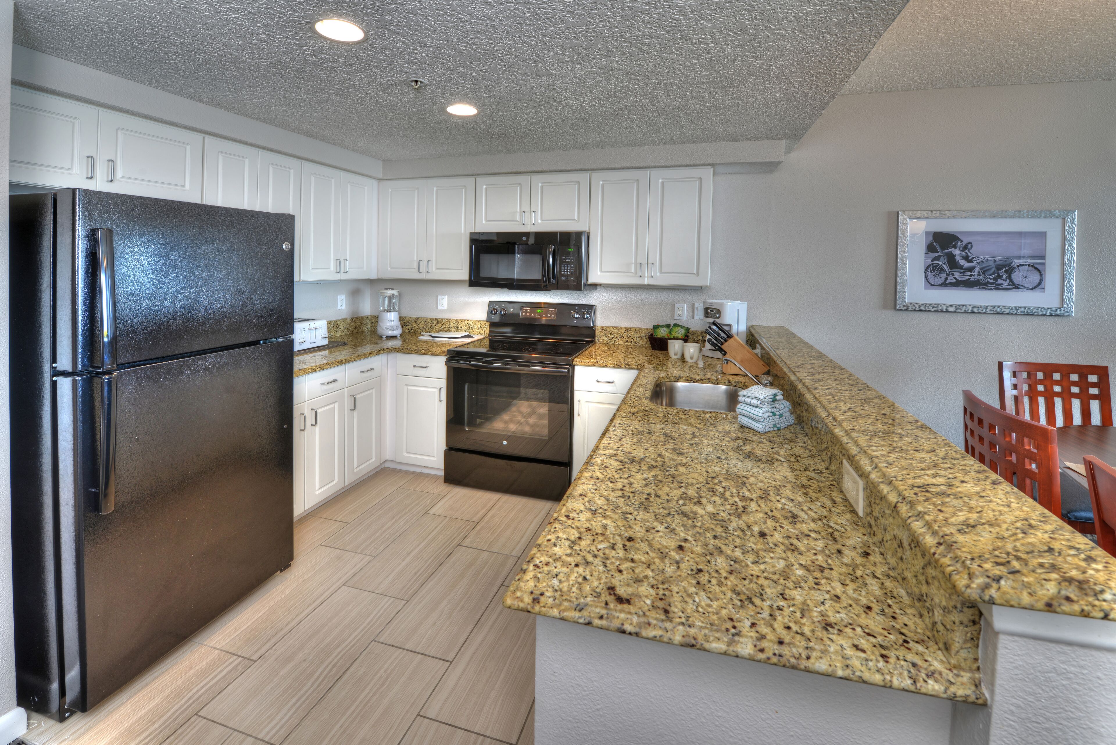 Una cocina moderna con armarios blancos, encimera de granito, electrodomésticos de acero inoxidable y un cuadro en la pared.