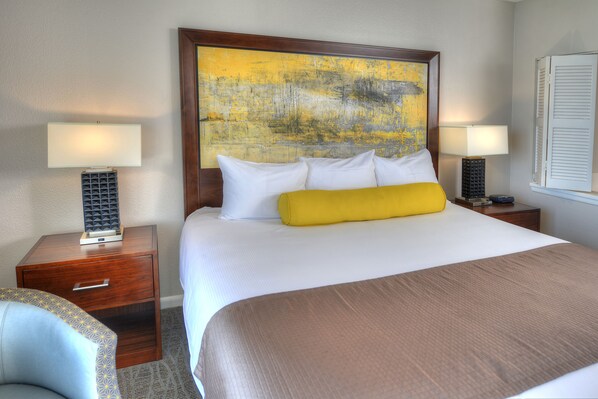 A hotel room with a large bed, two bedside tables with lamps, a wooden headboard, and a patterned chair.