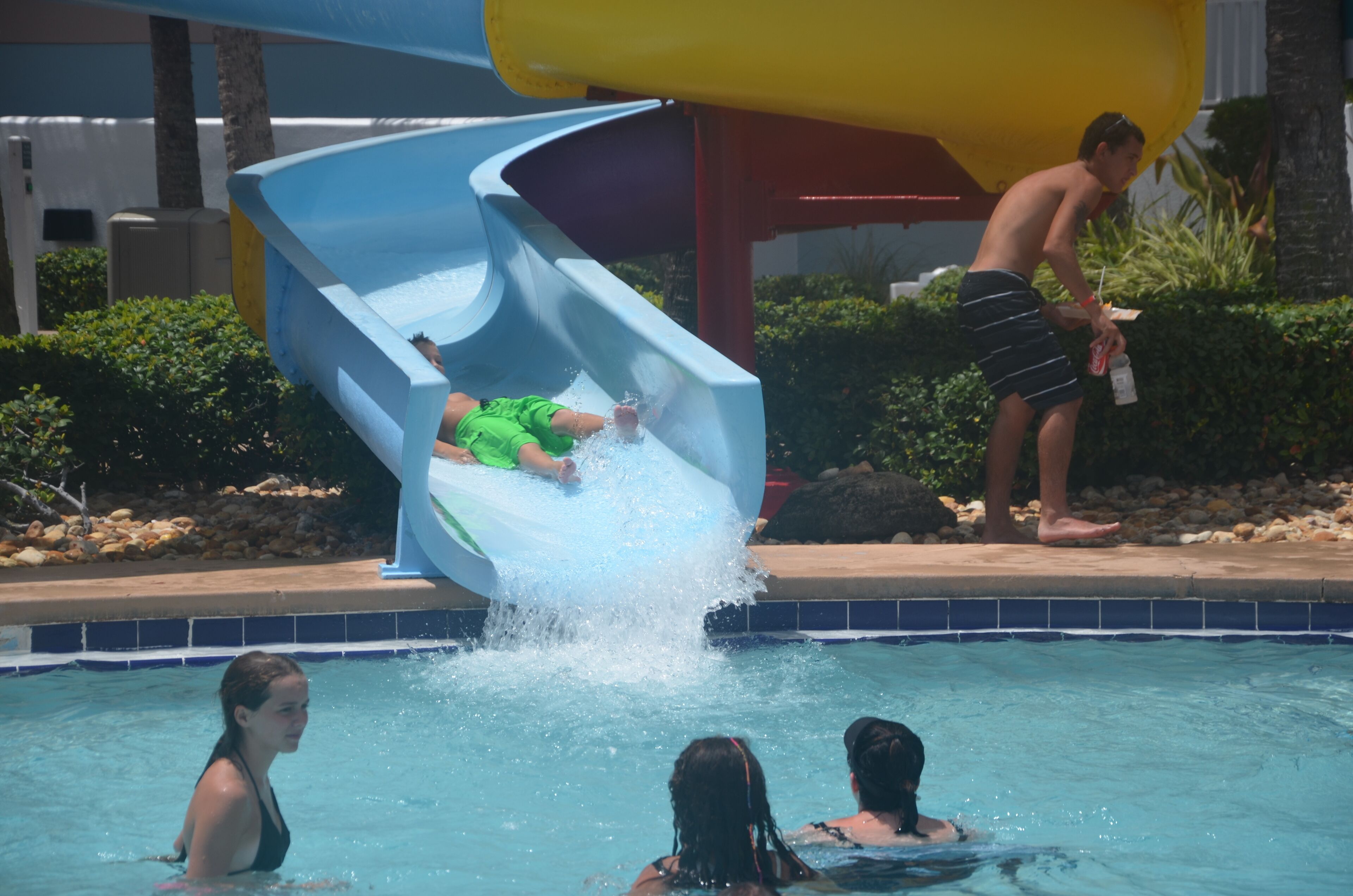 Tobogán de agua en una zona de piscina con gente disfrutando.