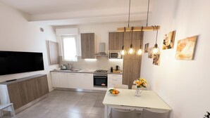 Eine moderne Küche mit Flachbildfernseher, Holzausstattung, Essbereich mit Tisch und Stühlen sowie Pendelleuchten.