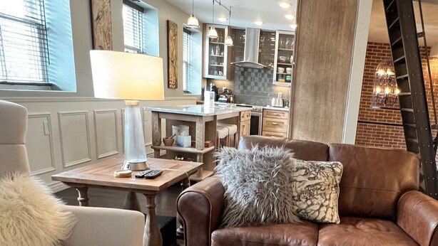 A cozy living room with a brown leather sofa, a wooden coffee table, and a lamp. - Loft on Mountain (in Old Town) (Fort Collins)