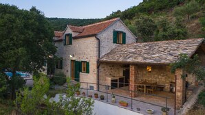 A stone house with a tiled roof and green shutters, surrounded by lush greenery and a pool. - Villa Dol-Three Bedroom Villa with Pool (Postira)