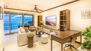 Un soggiorno moderno con divano, tavolino e televisore, con vista su un balcone e l'oceano.