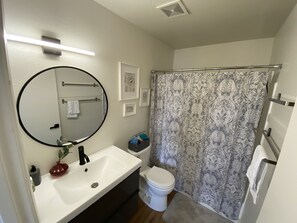 Bathroom features a white sink, black faucet, round mirror, and toilet, with a shower area and storage space.