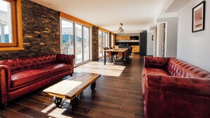 Un vaste espace de vie agrémenté d’un canapé en cuir rouge, d’une table basse en bois et d’un mur en pierre.