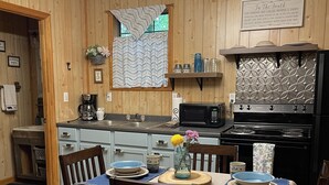 A cozy kitchen with wooden walls, a chandelier, a dining table set with plates and a vase of flowers, and a microwave and stove. - 1 Playful Cub-GREAT unbelievable rates, check it out (Cosby)