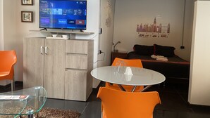 Un soggiorno moderno con televisore, mobiletto in legno, poltrone arancioni e un letto con un'opera d'arte raffigurante uno skyline urbano.
