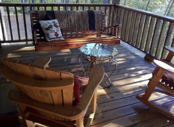 Una terraza de madera con una mecedora, un banco y una mesita.