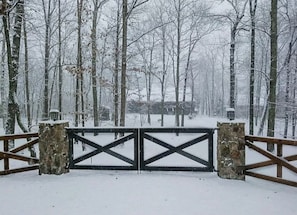 Stately entrance with stone pillars and a wooden fence, set amidst a serene winter landscape.
