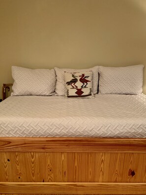 Un lit avec un matelas matelassé et deux oreillers, dont l’un est orné d’un motif décoratif.