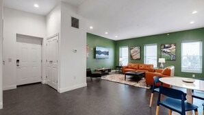 Una sala de estar moderna con una pared de acento verde, un área de comedor con mesa blanca y una disposición de asientos que incluye un sofá y sillones.