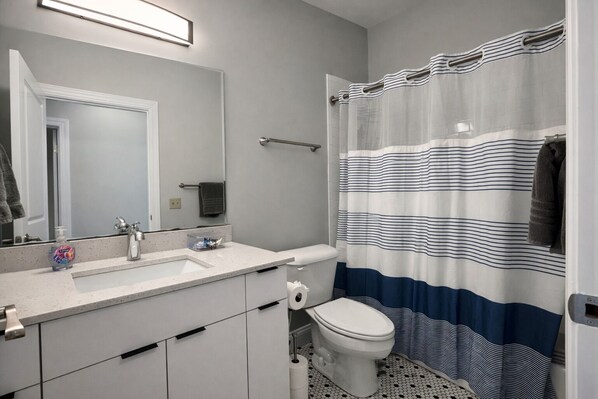A bathroom with a white sink, mirror, and toilet. There is a striped shower curtain and a towel rack.