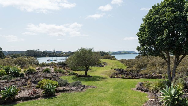 A landscaped garden with a pathway leading to a body of water, surrounded by various plants and trees. - Northern Lodge - cottage in a quiet rural setting, lush tropical gardens (Kerikeri)