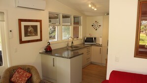 A compact kitchen with a central island, a microwave, and a window above the sink. - Northern Lodge - cottage in a quiet rural setting, lush tropical gardens (Kerikeri)