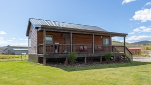 A two-story wooden building with a balcony, surrounded by a grassy lawn. - Spotted Moon Ranch - River Front - Two Bedroom Cabin (Etna)