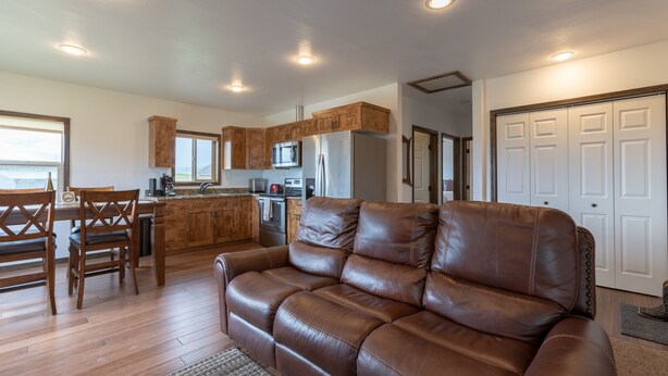 A modern kitchen with wooden cabinets, a dining area with a table and chairs, and a leather sofa in a living area. - Spotted Moon Ranch - River Front - Two Bedroom Cabin (Etna)