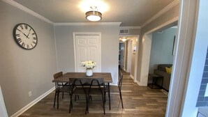 A dining area with a wooden table and chairs, a clock on the wall, and a door in the background. - Steps away from the BEACH! (Hilton Head Island)