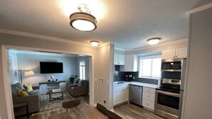 A modern open-plan living and kitchen area with a flat-screen TV mounted on the wall, wooden flooring, and built-in cabinetry. - Steps away from the BEACH! (Hilton Head Island)