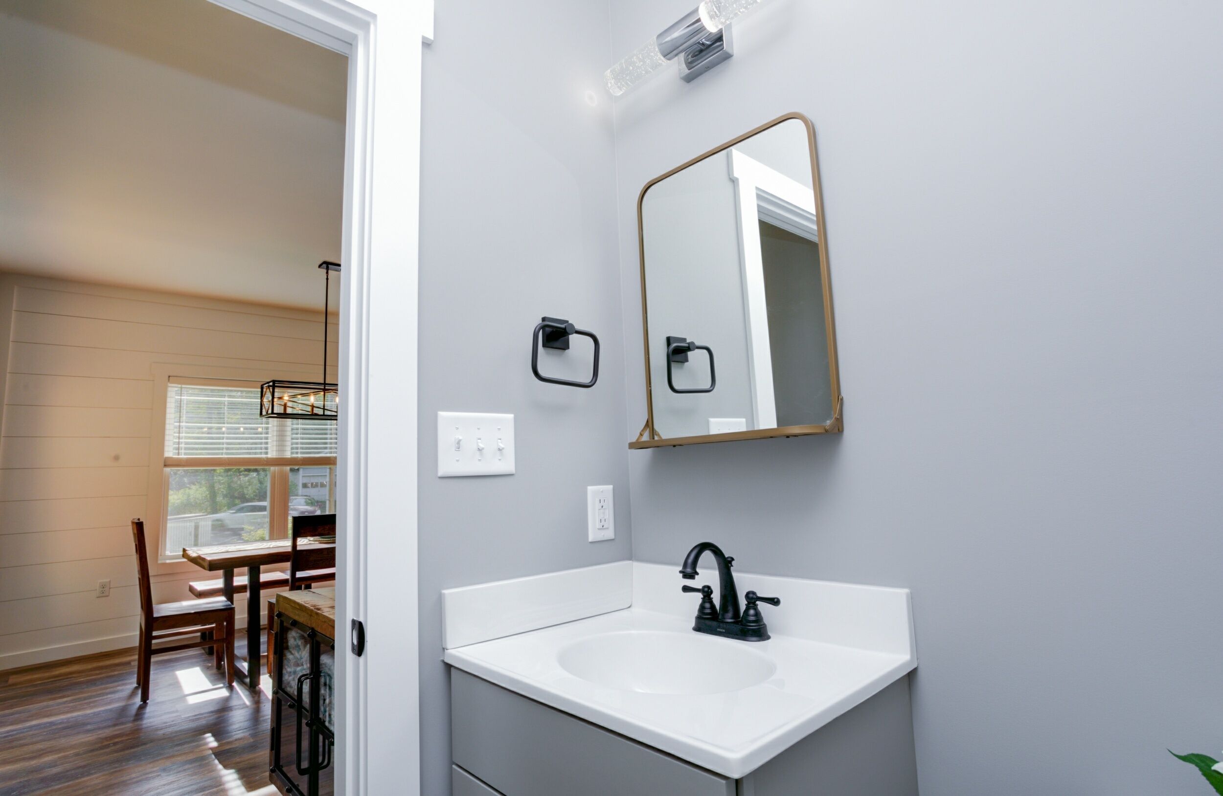 A bathroom with a white sink, black faucet, and a large mirror with a gold frame.