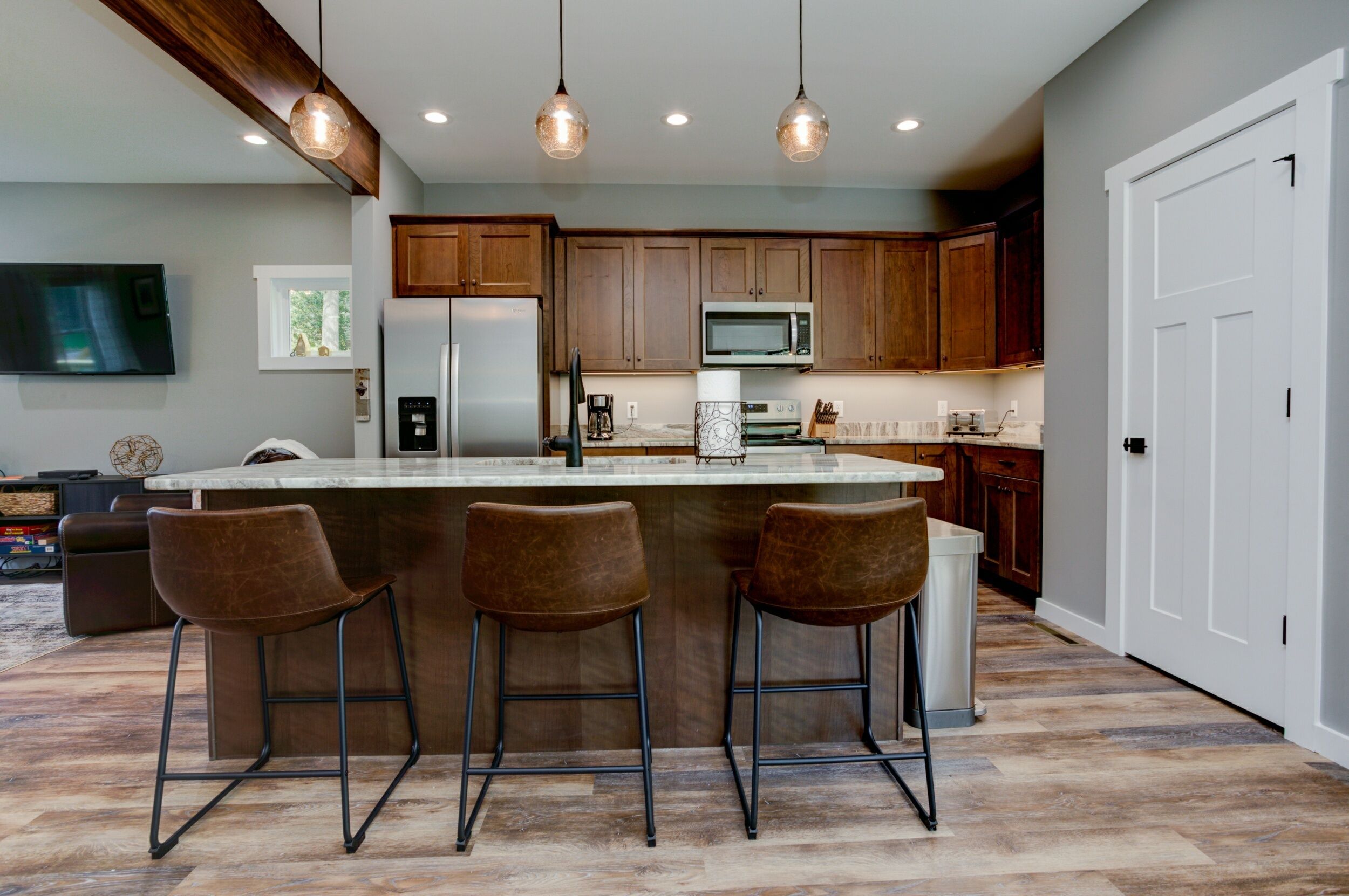 A modern kitchen with wooden cabinets, a central island with bar stools, a stainless steel refrigerator, and a microwave.