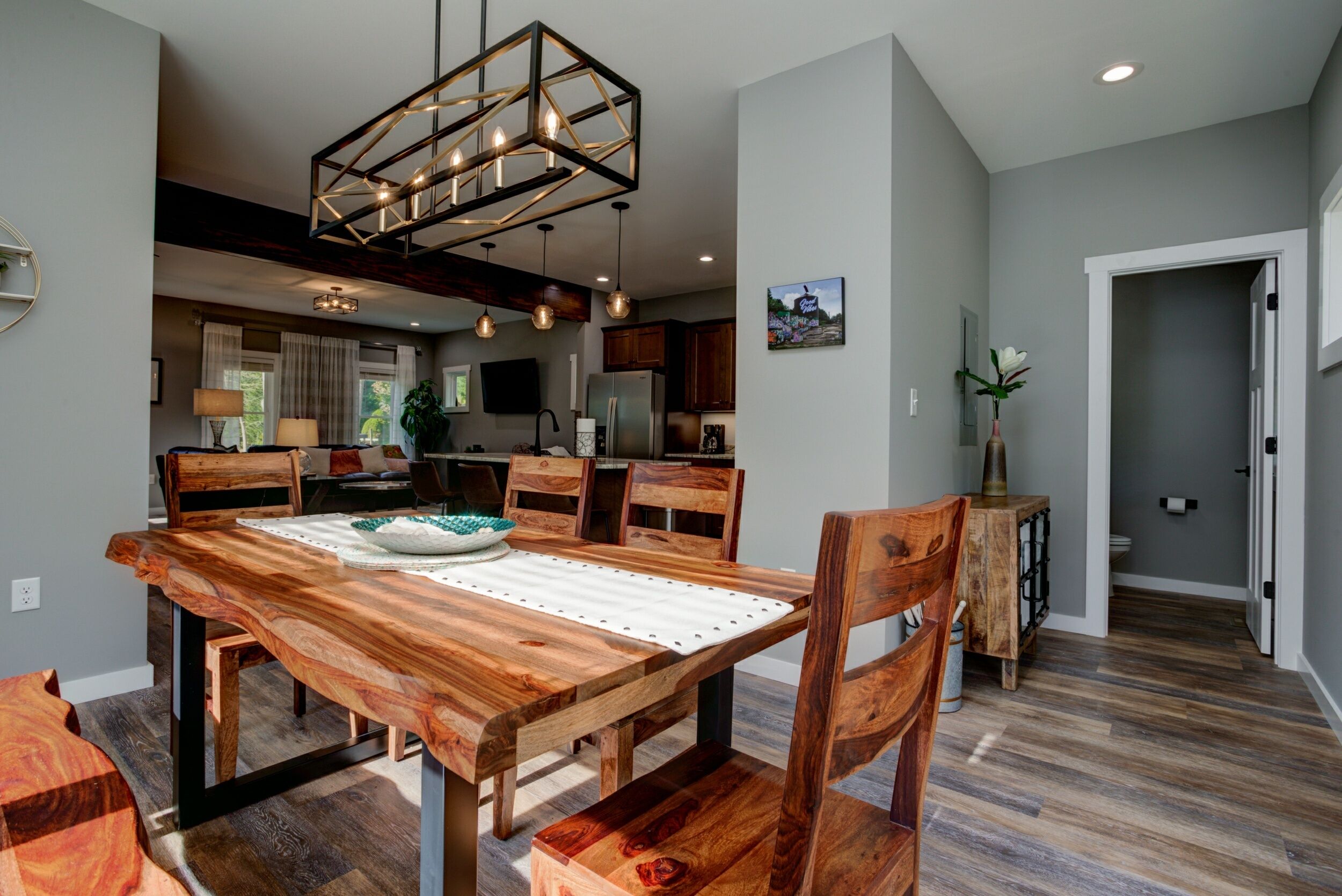Un vaste espace dédié à la salle à manger, avec une table et des chaises en bois, une cuisine moderne en arrière-plan et un couloir menant à une autre pièce.