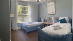 Un dormitorio con dos camas, una ventana con cortinas, un cuadro en la pared y un ventilador de techo.