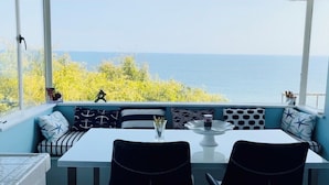 A dining area with a table and chairs, a view of the sea, and a window with a view of trees. - Beach house with unforgettable view (Los Angeles)