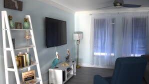 Een woonkamer met een televisie, een blauwe fauteuil, een witte trap en een boekenkast met decoratieve objecten.