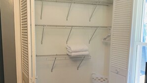 Een inloopkast met openslaande deuren, houten vloer en een witte wasmand.