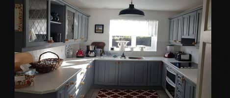 A kitchen with grey cabinets, a black pendant light, a window with white curtains, and a patterned rug.