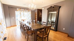 Une salle à manger avec une table et des chaises en bois, un lustre et un grand miroir au mur.