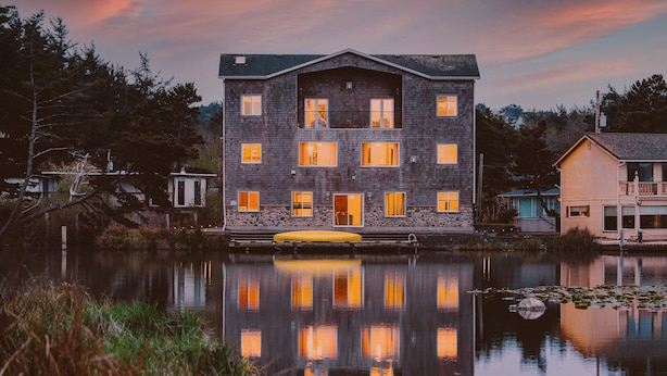 Un immeuble à plusieurs étages, doté de nombreuses fenêtres qui se reflètent dans une étendue d’eau calme, et entouré d’arbres et d’un autre bâtiment.