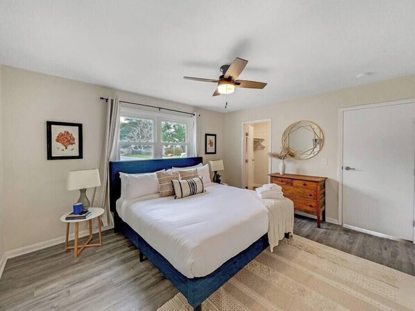 A bedroom with a bed, a ceiling fan, a dresser, a mirror, and a window.