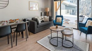 A modern living room with a sofa, two armchairs, a dining table with chairs, a coffee table, and a view of a snowy landscape through large windows. - Superb 88m2 flat, 3 bedrooms, 2 bathrooms, at the foot of the pistes (Châtel)