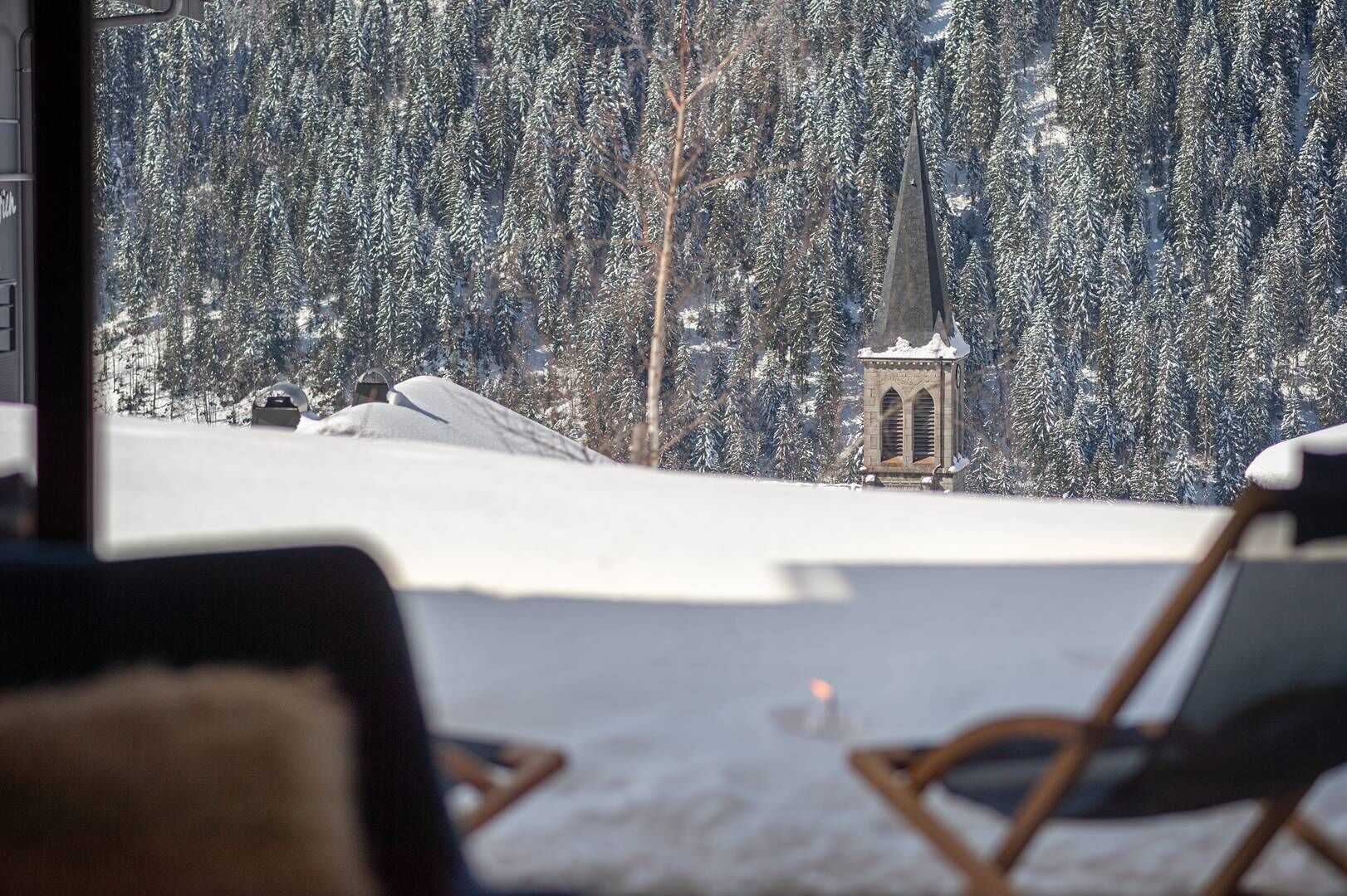Schneebedeckte Landschaft mit einem Kirchturm und einem Stuhl im Vordergrund.