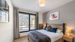 A bedroom with a large bed, a nightstand, a lamp, a window with curtains, and a framed picture on the wall. - Superb 88m2 flat, 3 bedrooms, 2 bathrooms, at the foot of the pistes (Châtel)