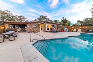 A backyard with a swimming pool, picnic table, and barbecue grill.