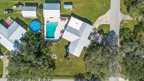 An aerial view of a residential property with a swimming pool, multiple buildings, and surrounding greenery.