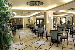 Um hall de hotel com piso de azulejos, várias áreas de estar e uma mesa de recepção.