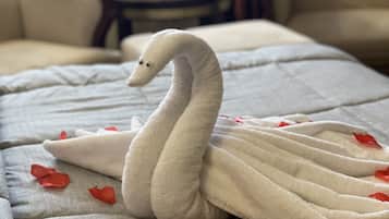 Una toalla con forma de cisne sobre una cama con pétalos de rosa roja esparcidos.