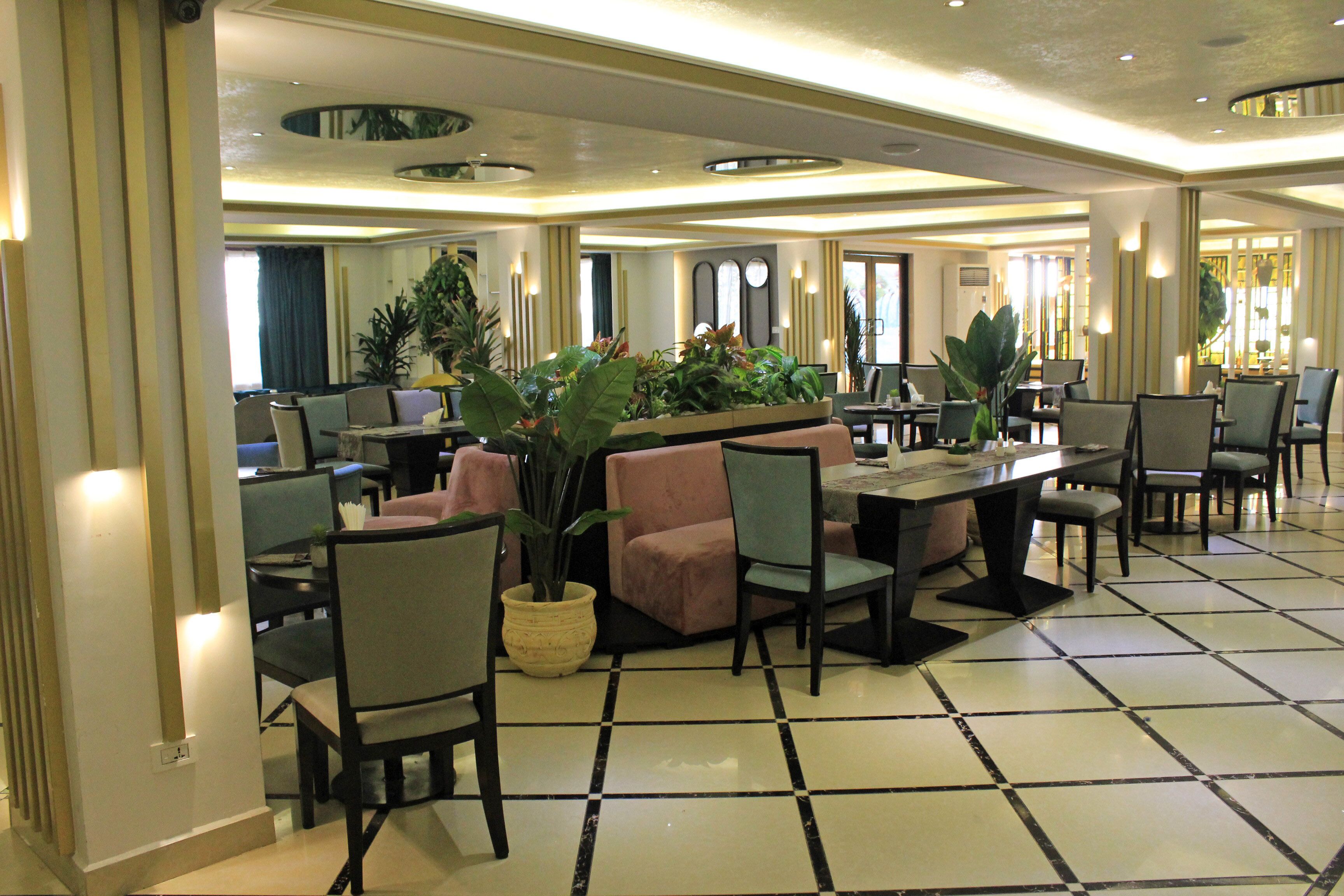 Un hall de hotel con piso a cuadros, varias zonas de estar y plantas en macetas.