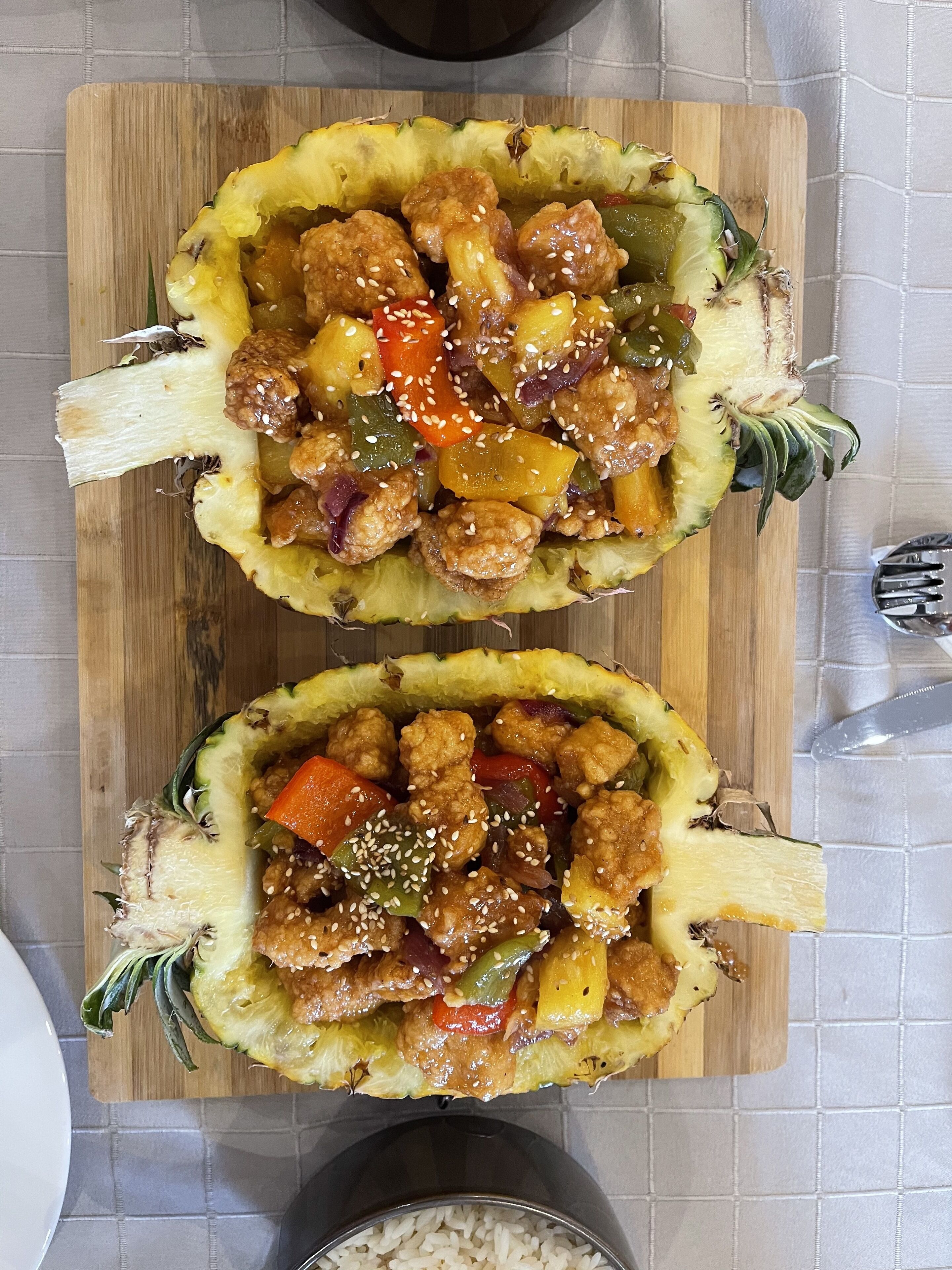Una tabla de madera con dos mitades de piña rellenas de un plato de pollo y verduras.