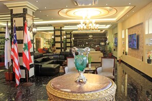 A lobby with a chandelier, flags, a green vase, and a sofa. - Boulevard Palace Hotel (Monrovia)